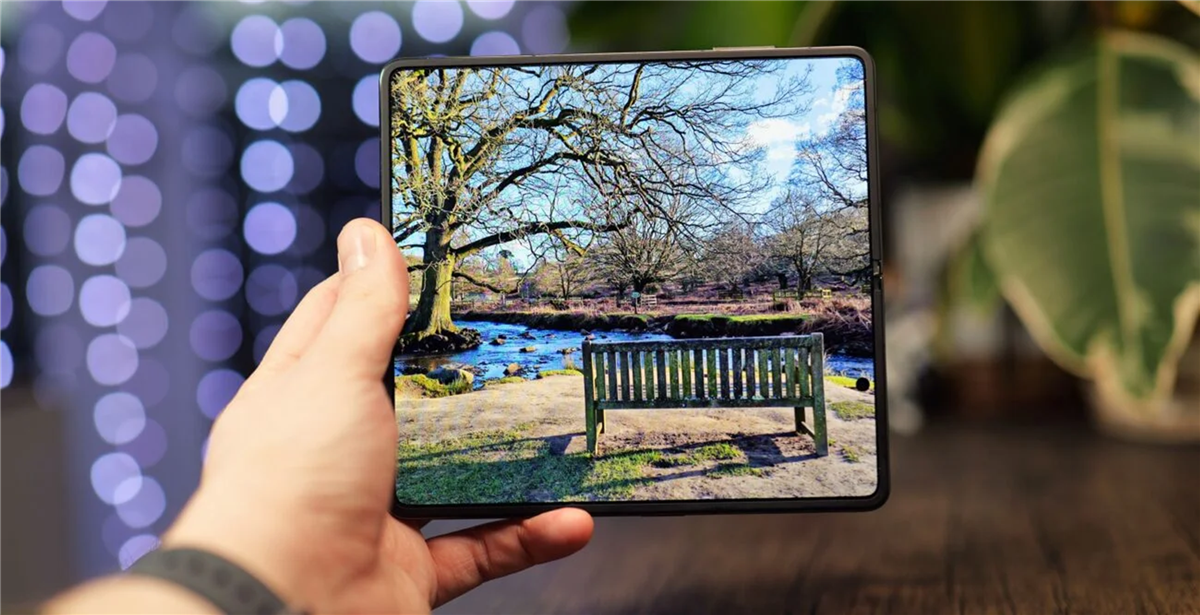 A hand holding a tablet with a bench and a pond

Description automatically generated